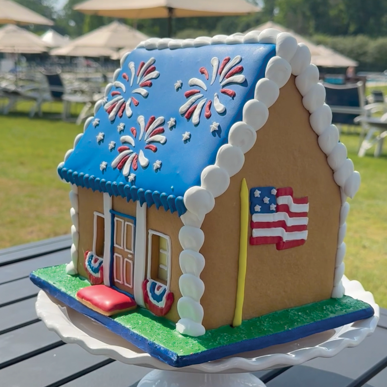 Gingerbread house with American flag and fireworks on a table outdoors