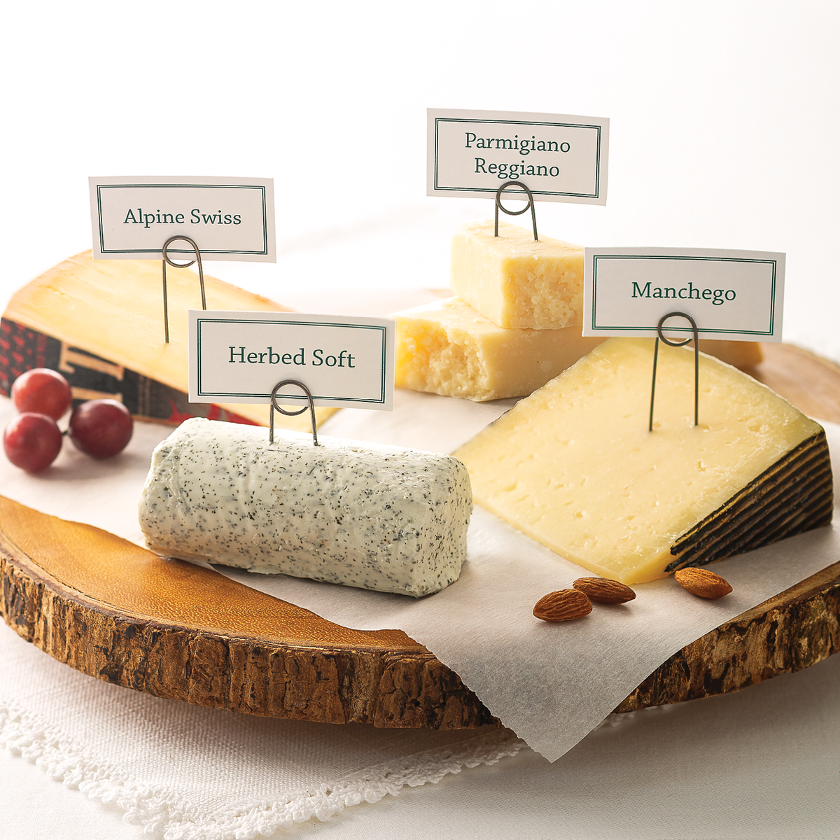 Reserve Cheese Collections on a wood slice tray. The Apline Swiss Cheese, the Parmigiano Reggiano, Herbed Soft, and Manchego cheese.