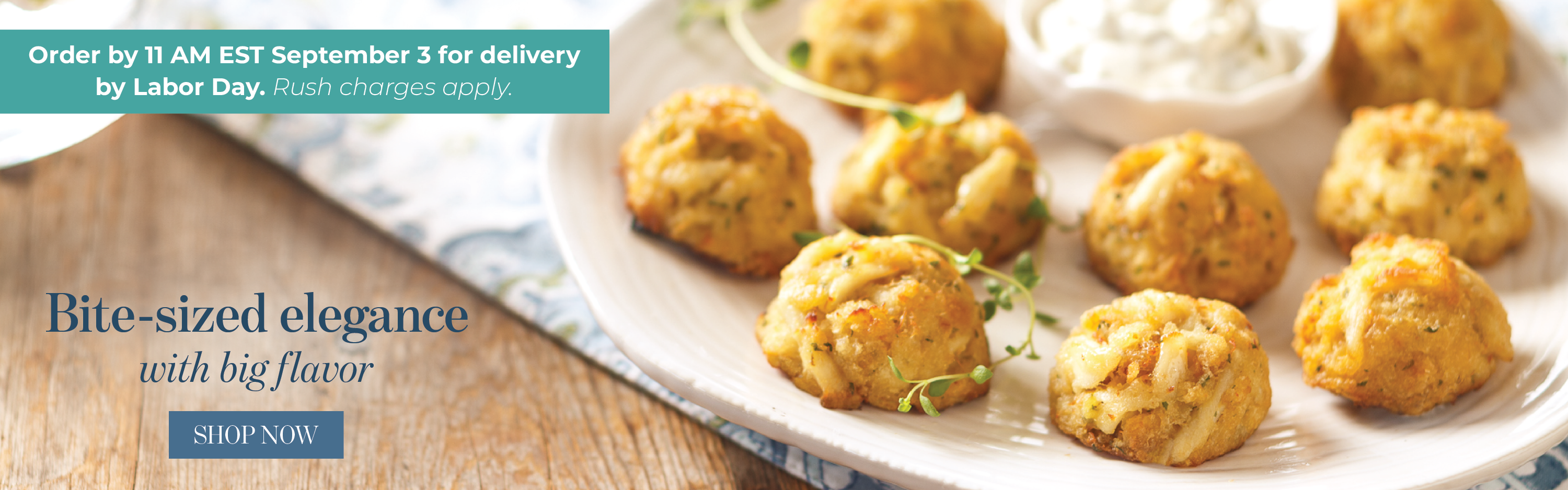 Bite-sized golden-brown baked crab cakes served on a white plate with a side of creamy white sauce, set on a wooden table with text that reads Bite-size elegance with big flavor. Shop crab cakes. Order by 11am on September 3 for delivery by Labor Day.